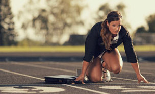 Eine Sportökonomin wartet im Business Dress in einer Starterposition auf einem Sportplatz