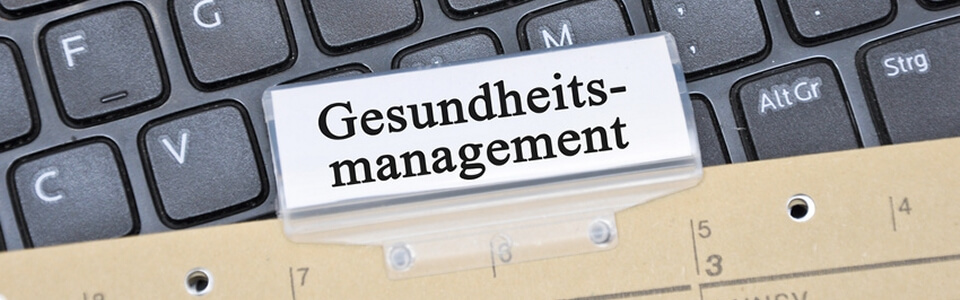 Nahaufnahme einer Akte, die mit "Gesundheitsmanagement" beschriftet ist und auf einer Tastatur liegt