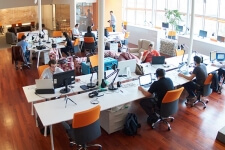 Aufnahme eines Großraumbüros mit vielen Arbeitsplätzen, von denen circa die Hälfte belegt ist