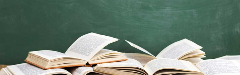 Mehrere aufgeschlagene Bücher liegen vor einer leeren Schultafel