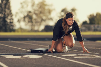 Eine Sportökonomin wartet im Business Dress in einer Starterposition auf einem Sportplatz