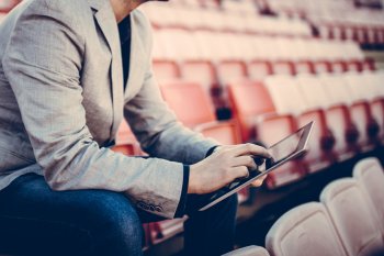 Sportmanager sitzt mit Tablet auf leerer Tribüne