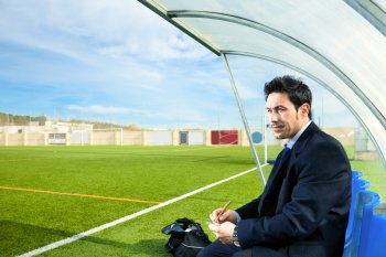 Sportmanager sitzt an Fußballfeld und macht sich Notizen